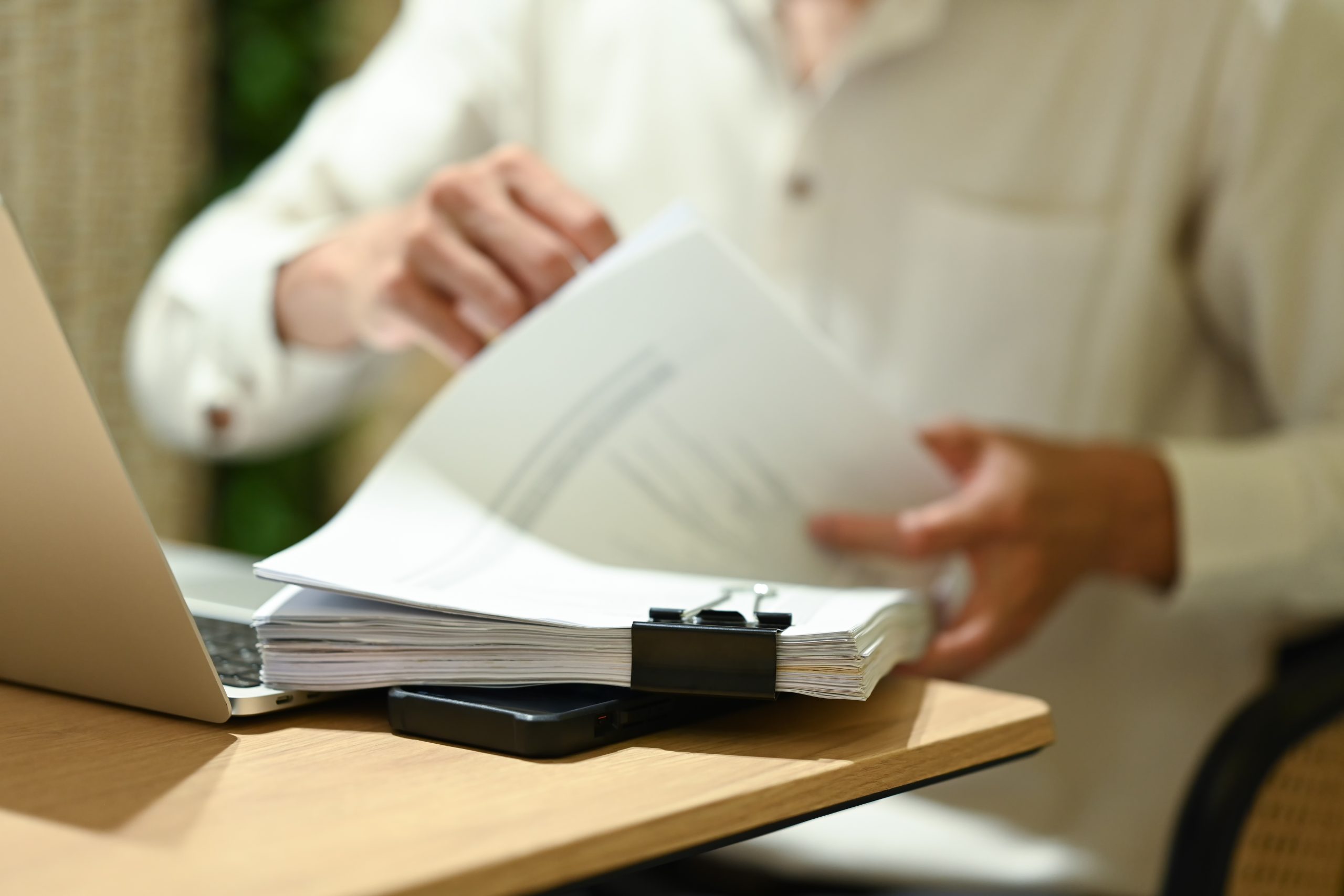 Unrecognizable businessman sitting in front of laptop and working with documents on wooden office desk